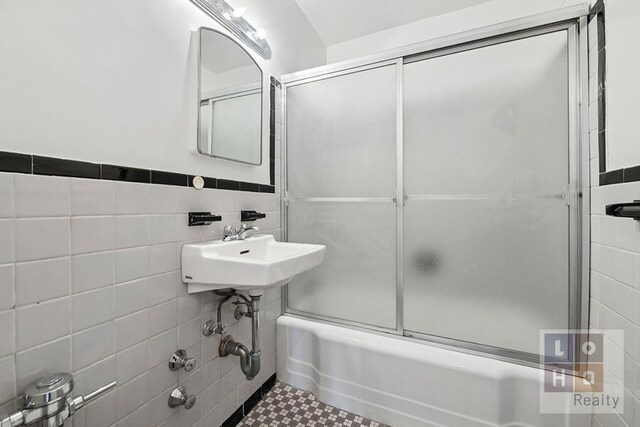 577 Grand St Unit F1904, New York City, NY 10002 - bathroom featuring tile walls, combined bath / shower with glass door, a sink, wainscoting, and tile patterned flooring