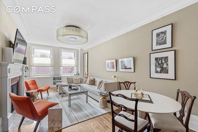 living room featuring a brick fireplace, light wood finished floors, and crown molding