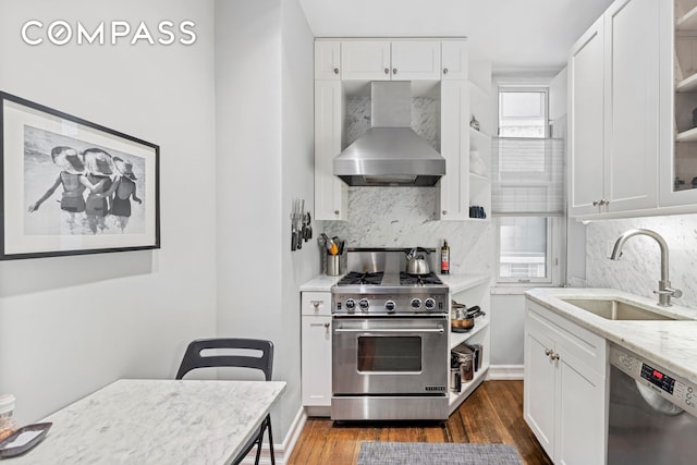 kitchen featuring white cabinets, appliances with stainless steel finishes, dark wood-style flooring, wall chimney range hood, and a sink