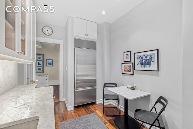 kitchen with built in fridge, dark wood-style flooring, white cabinetry, light countertops, and glass insert cabinets