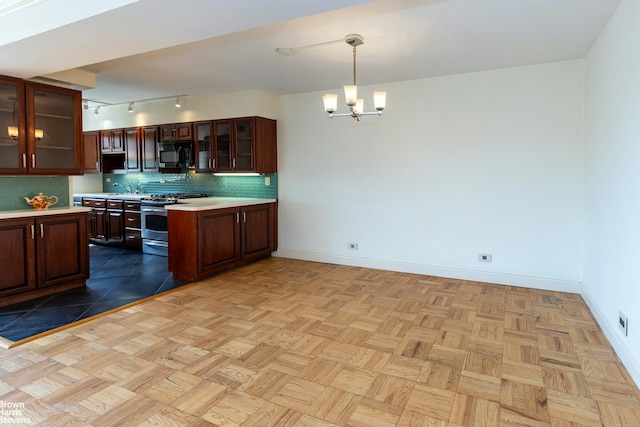 kitchen with tasteful backsplash, an inviting chandelier, black microwave, light countertops, and stainless steel range with gas stovetop