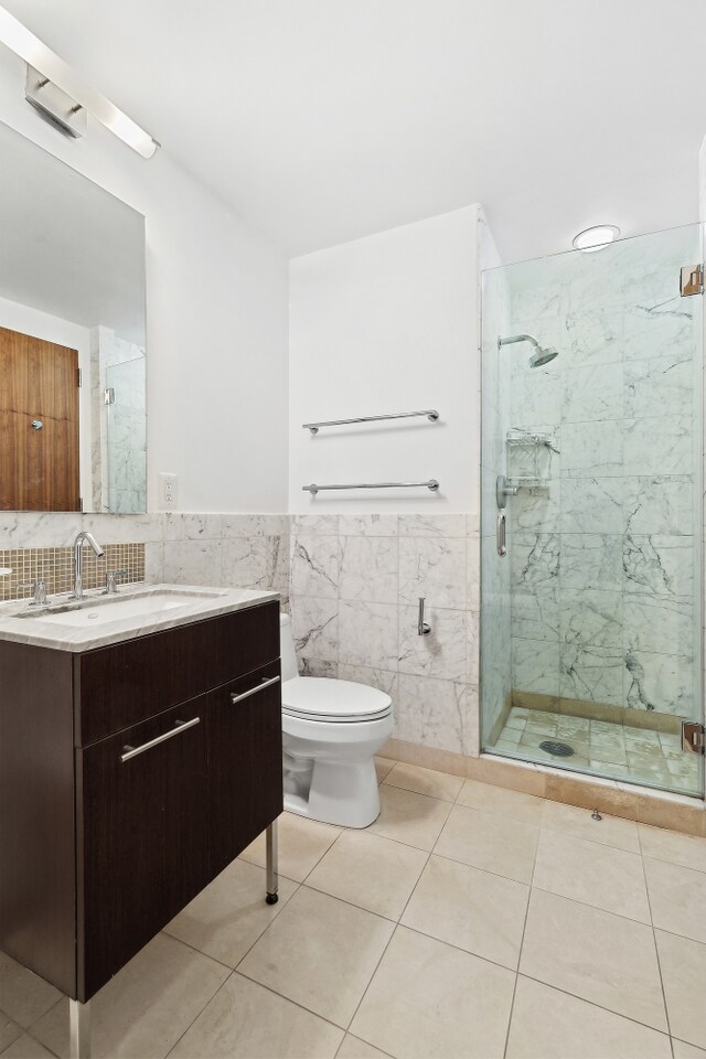 bathroom with tile patterned flooring, a marble finish shower, vanity, and tile walls