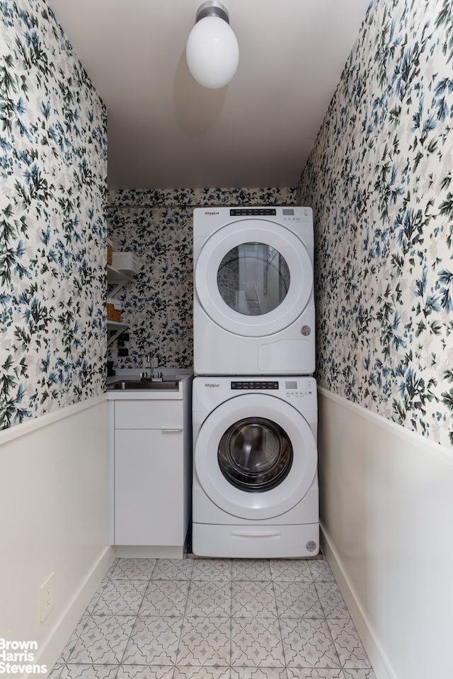 clothes washing area with stacked washer and dryer, wainscoting, a sink, and wallpapered walls