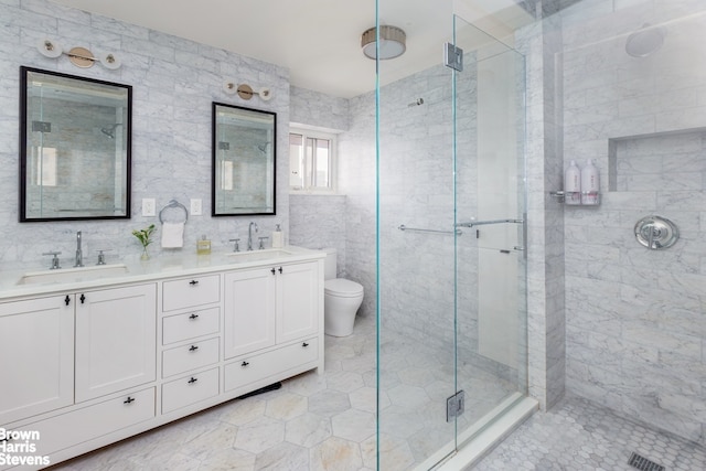 bathroom with double vanity, a stall shower, toilet, and a sink