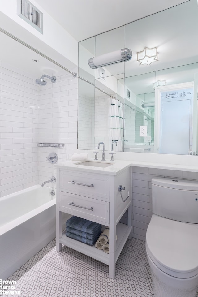 full bath featuring toilet, vanity, visible vents, tile walls, and shower / bath combo