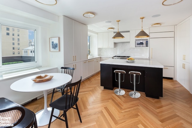 kitchen with light countertops, hanging light fixtures, white cabinets, a kitchen island, and built in appliances