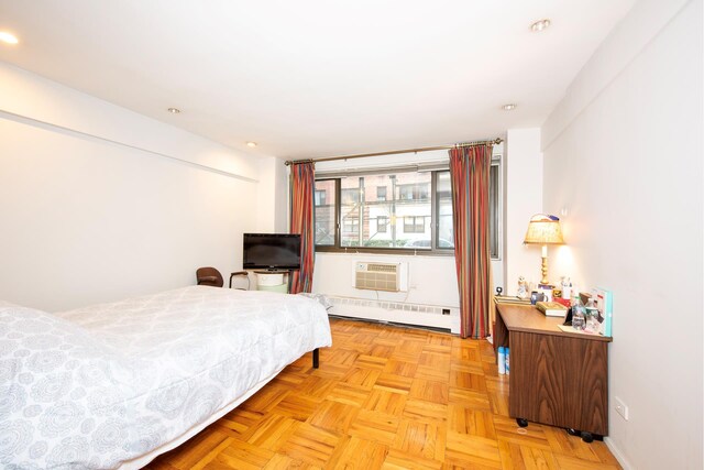 bedroom with baseboard heating, light parquet flooring, and an AC wall unit