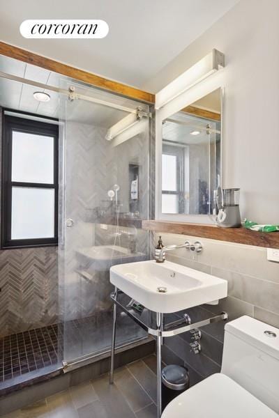 bathroom with tile patterned flooring, a shower stall, toilet, tile walls, and a sink