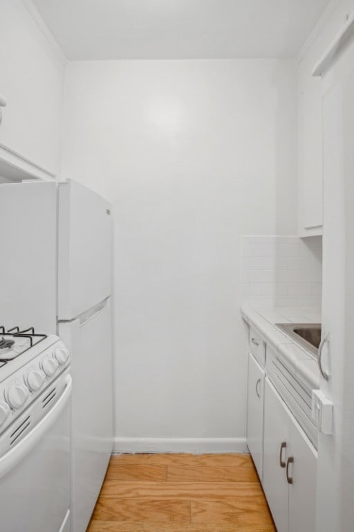 kitchen featuring white cabinetry, ornamental molding, white appliances, light hardwood / wood-style floors, and backsplash