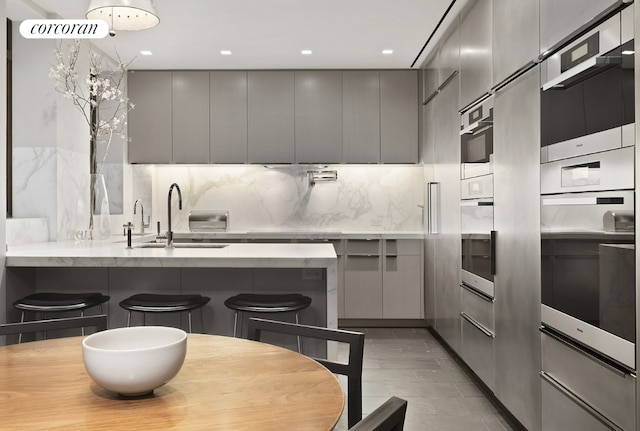 kitchen with gray cabinets, sink, a breakfast bar area, and oven