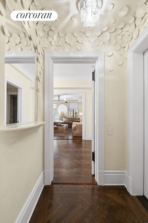 corridor with an inviting chandelier, crown molding, and dark parquet floors