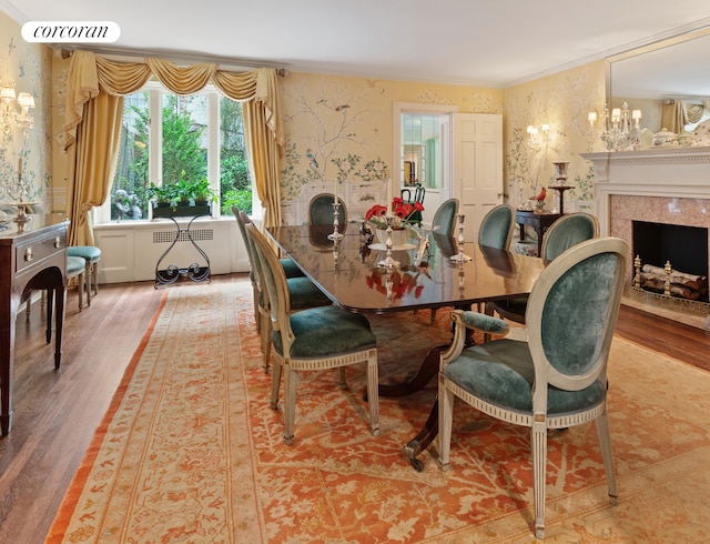 dining area featuring crown molding, radiator heating unit, a premium fireplace, wood finished floors, and wallpapered walls