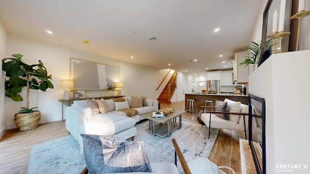 living area featuring visible vents, baseboards, stairway, light wood-type flooring, and recessed lighting