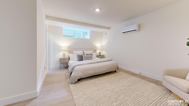 bedroom with baseboards, light wood finished floors, and a wall mounted AC