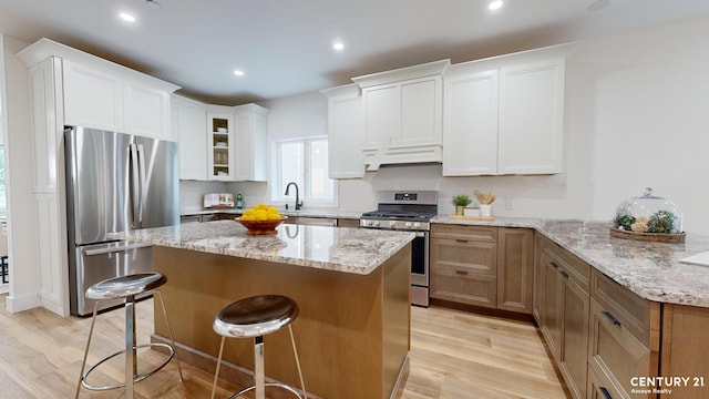 kitchen featuring a kitchen bar, light wood-style flooring, a sink, light stone counters, and appliances with stainless steel finishes