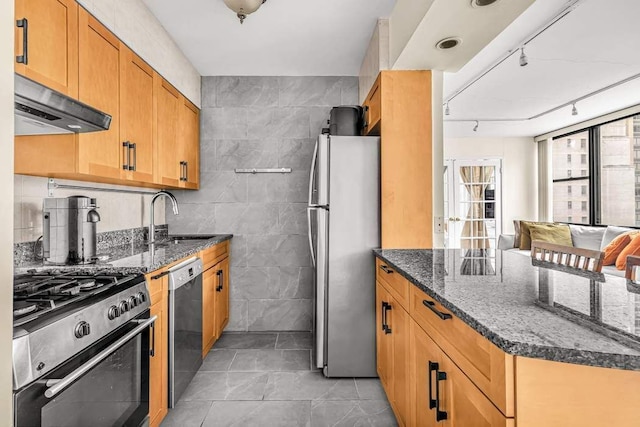 kitchen featuring sink, tile walls, dark stone counters, stainless steel appliances, and track lighting