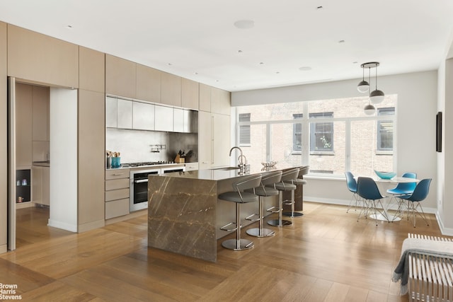 kitchen featuring a breakfast bar area, baseboards, decorative light fixtures, backsplash, and a center island with sink