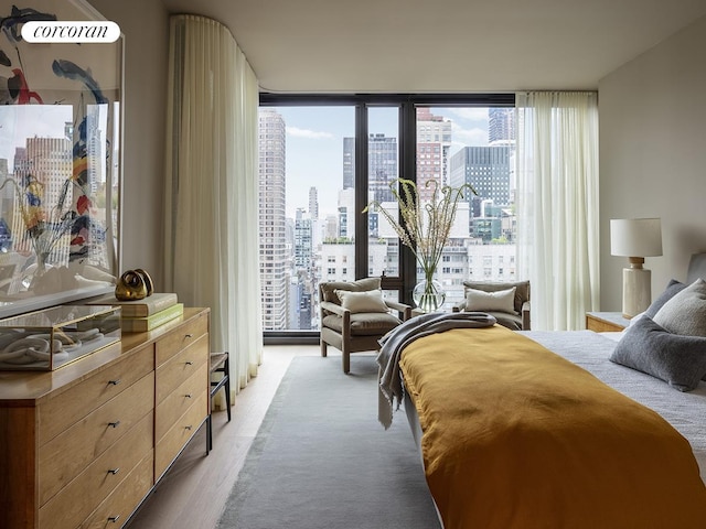 bedroom featuring light wood-style floors, a view of city, and expansive windows