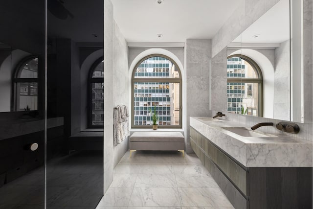 full bath featuring marble finish floor, double vanity, and a healthy amount of sunlight