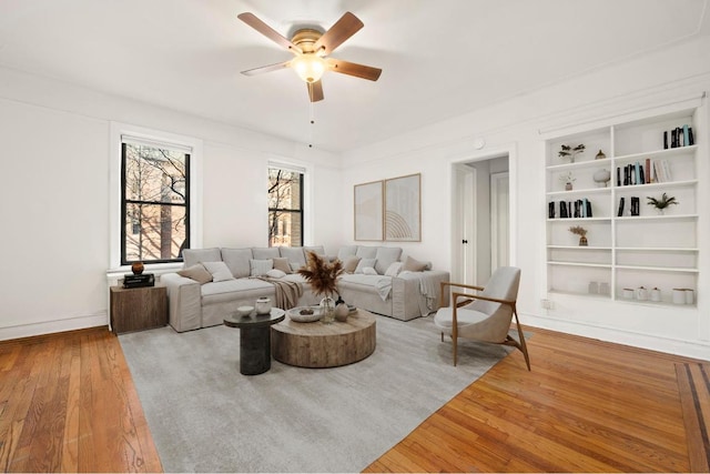 living room with built in shelves, ceiling fan, and hardwood / wood-style floors