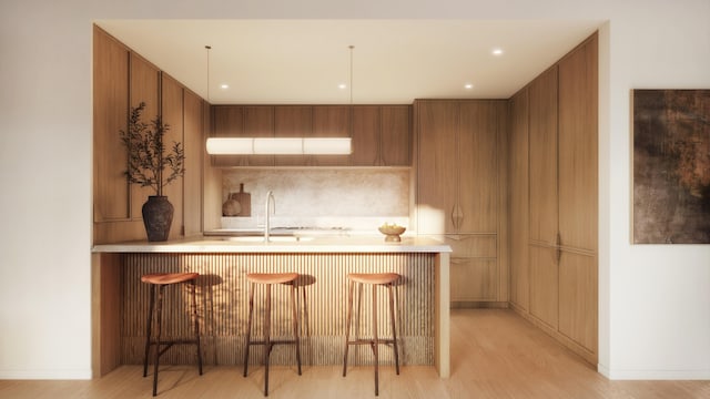 kitchen featuring brown cabinetry, light countertops, light wood-type flooring, a kitchen bar, and a sink