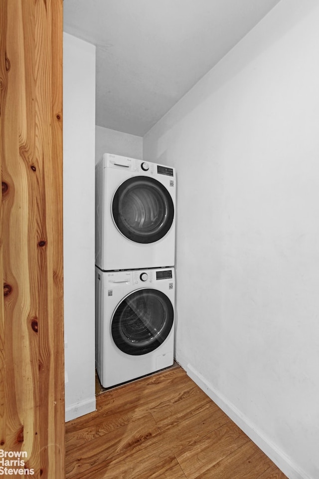 washroom featuring stacked washer / dryer, baseboards, and wood finished floors