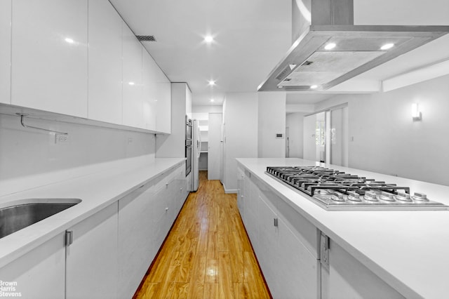 kitchen featuring white cabinets, light countertops, ventilation hood, light wood finished floors, and stainless steel gas stovetop