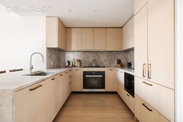 kitchen with light brown cabinetry, backsplash, and black appliances