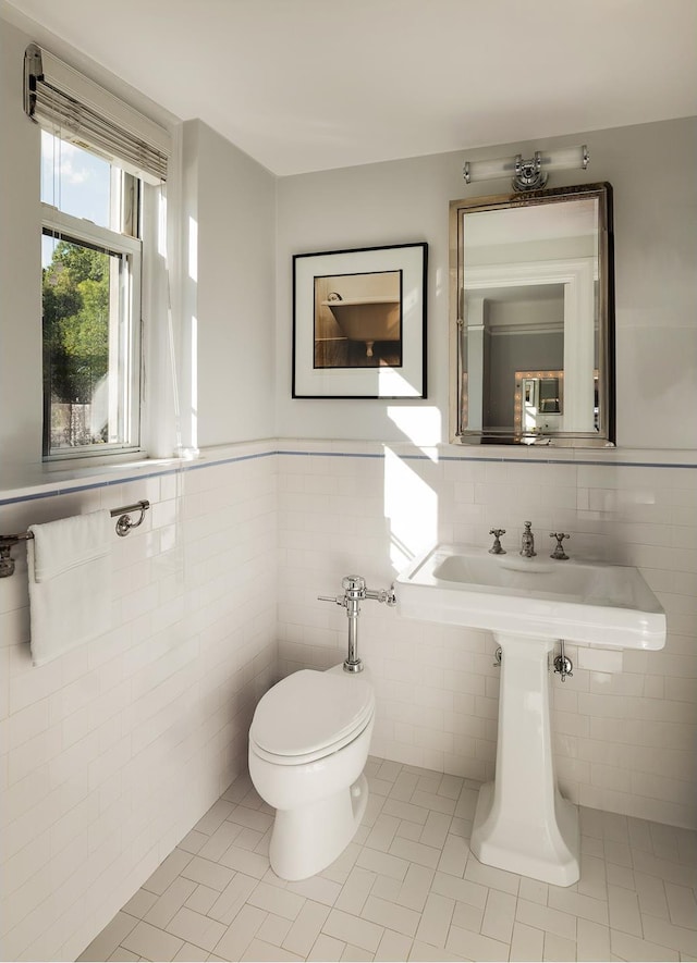 half bathroom with tile patterned floors, a wainscoted wall, toilet, and tile walls