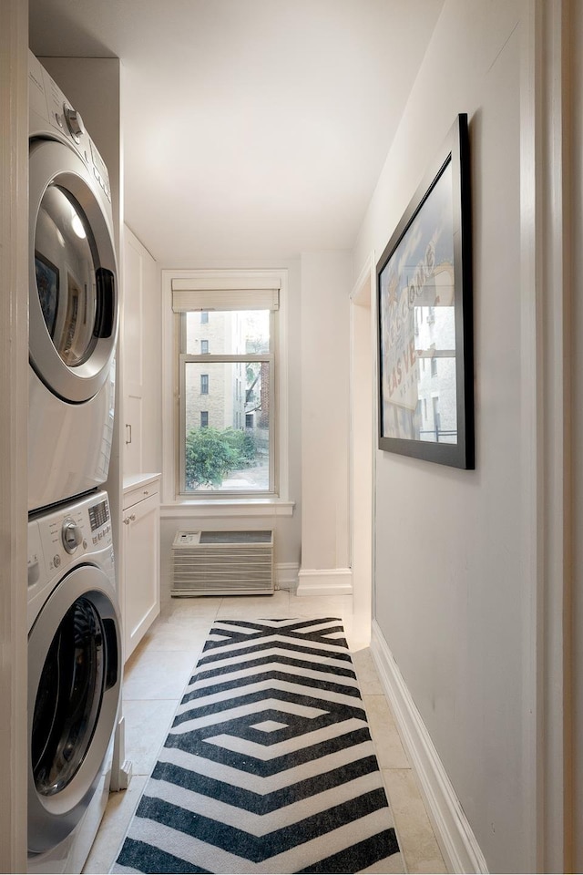 laundry room featuring stacked washer and dryer, a wall mounted AC, cabinet space, light tile patterned floors, and baseboards