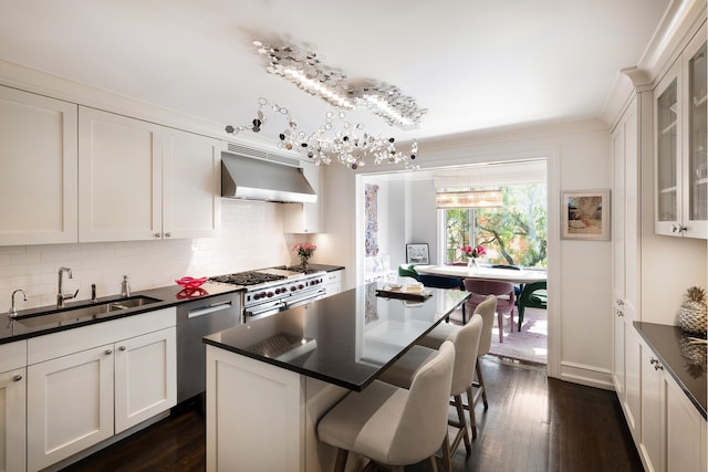 kitchen with dark countertops, under cabinet range hood, a breakfast bar, appliances with stainless steel finishes, and a sink