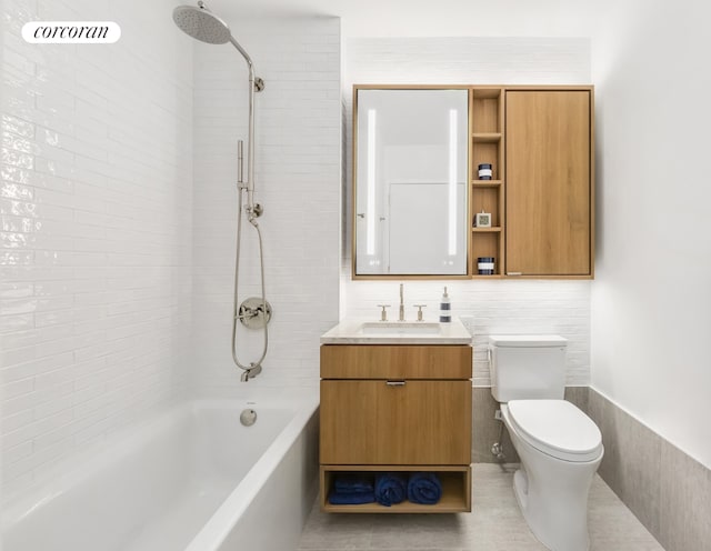 full bathroom featuring tile patterned floors, toilet, tiled shower / bath, tile walls, and vanity