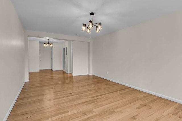 empty room featuring light wood-style flooring, baseboards, and a chandelier