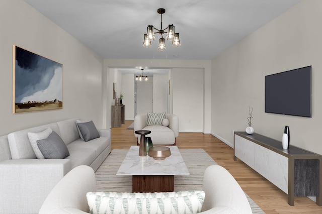 living room featuring light wood finished floors, a notable chandelier, and baseboards