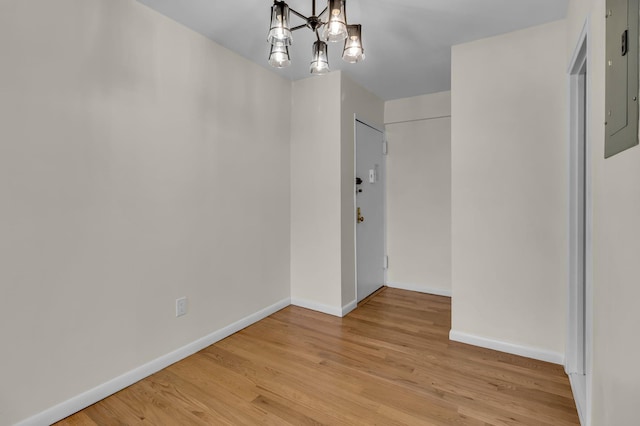 unfurnished dining area with electric panel, baseboards, a chandelier, and light wood finished floors