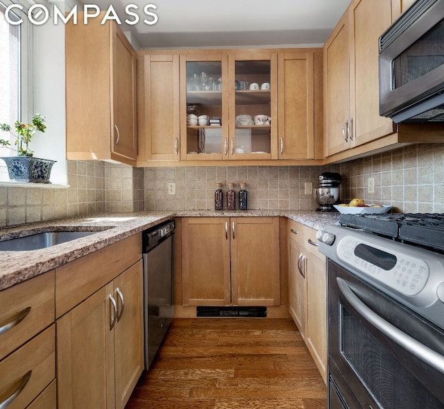 kitchen featuring dark wood-type flooring, appliances with stainless steel finishes, backsplash, light stone counters, and light brown cabinets