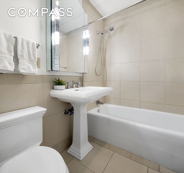 bathroom featuring tile patterned floors, toilet, tiled shower / bath combo, and tile walls