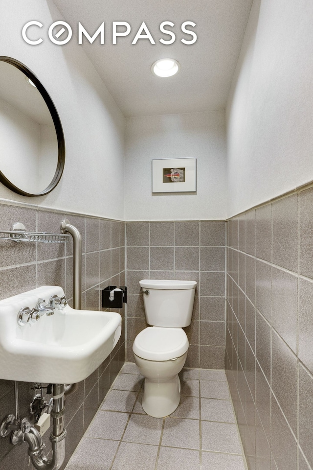 115 E 61st St Unit 1C, New York City, NY 10065 - bathroom featuring tile walls, toilet, wainscoting, a sink, and tile patterned flooring