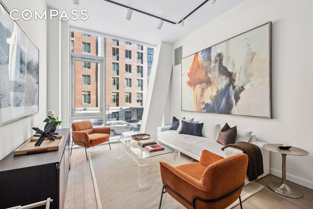 sitting room with expansive windows, track lighting, baseboards, and wood finished floors