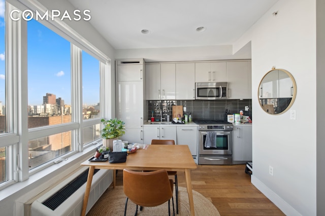 kitchen with light wood-style flooring, backsplash, radiator heating unit, appliances with stainless steel finishes, and baseboards