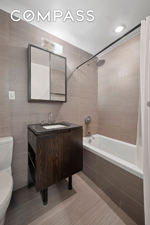 bathroom featuring tile patterned floors, toilet, tiled shower / bath combo, tile walls, and vanity