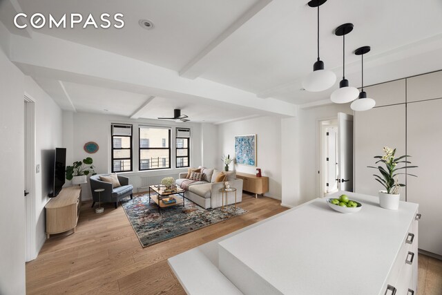 living area featuring light wood-style floors, beam ceiling, and ceiling fan