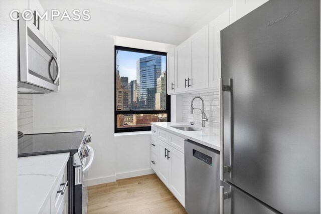240 E 47th St Unit 27A, New York City, NY 10017 - kitchen with light wood-type flooring, stainless steel appliances, a sink, white cabinets, and light stone countertops