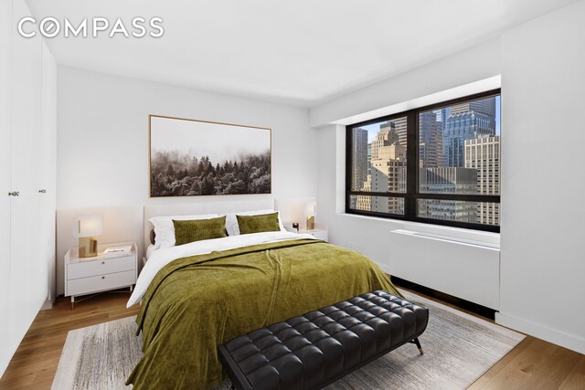 240 E 47th St Unit 27A, New York City, NY 10017 - bedroom featuring baseboards, wood finished floors, and a city view