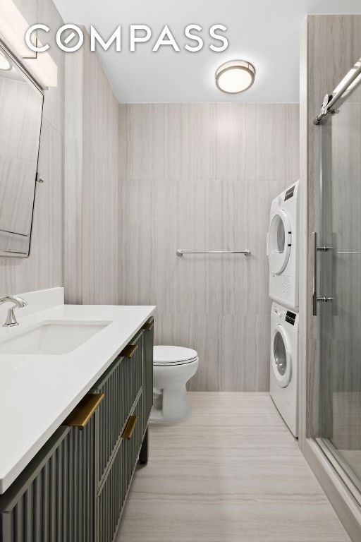 bathroom featuring stacked washer and dryer, toilet, an enclosed shower, tile walls, and vanity