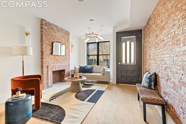 foyer with an inviting chandelier, brick wall, a fireplace, and light hardwood / wood-style flooring