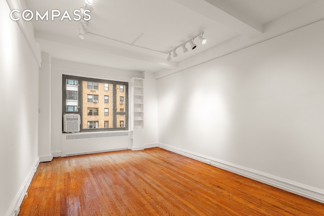 unfurnished room featuring radiator, track lighting, wood finished floors, and baseboards