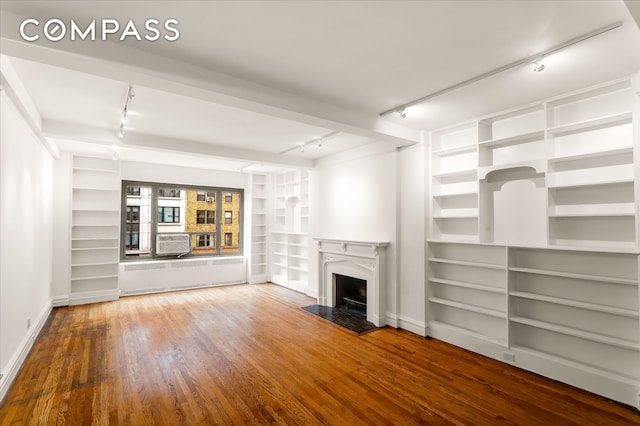 unfurnished living room featuring track lighting, radiator heating unit, a fireplace, built in features, and wood finished floors
