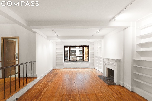 unfurnished living room featuring hardwood / wood-style floors, built in shelves, and track lighting