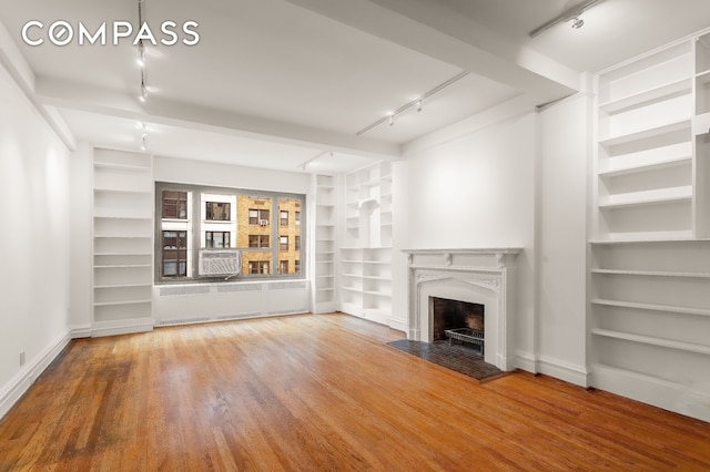 unfurnished living room featuring track lighting, radiator heating unit, built in shelves, wood finished floors, and baseboards